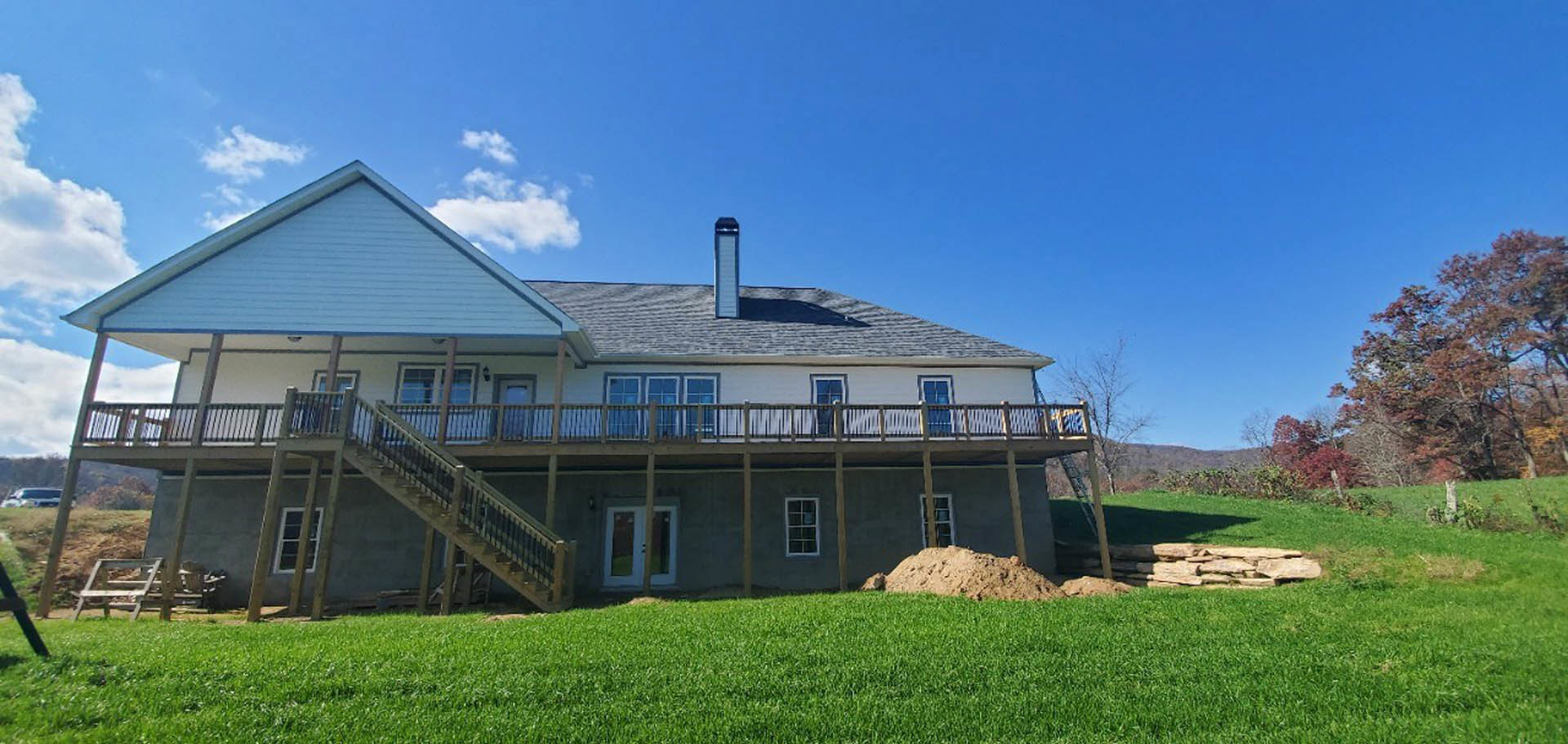 Two-story house with wood deck, white framed windows, large grassy yard, mature tree with red leaves, and cloudy sky in background