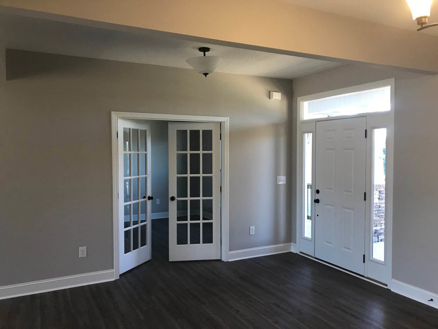 Double white doors with glass panes and black handles, dark wood flooring, white walls, ceiling light fixture