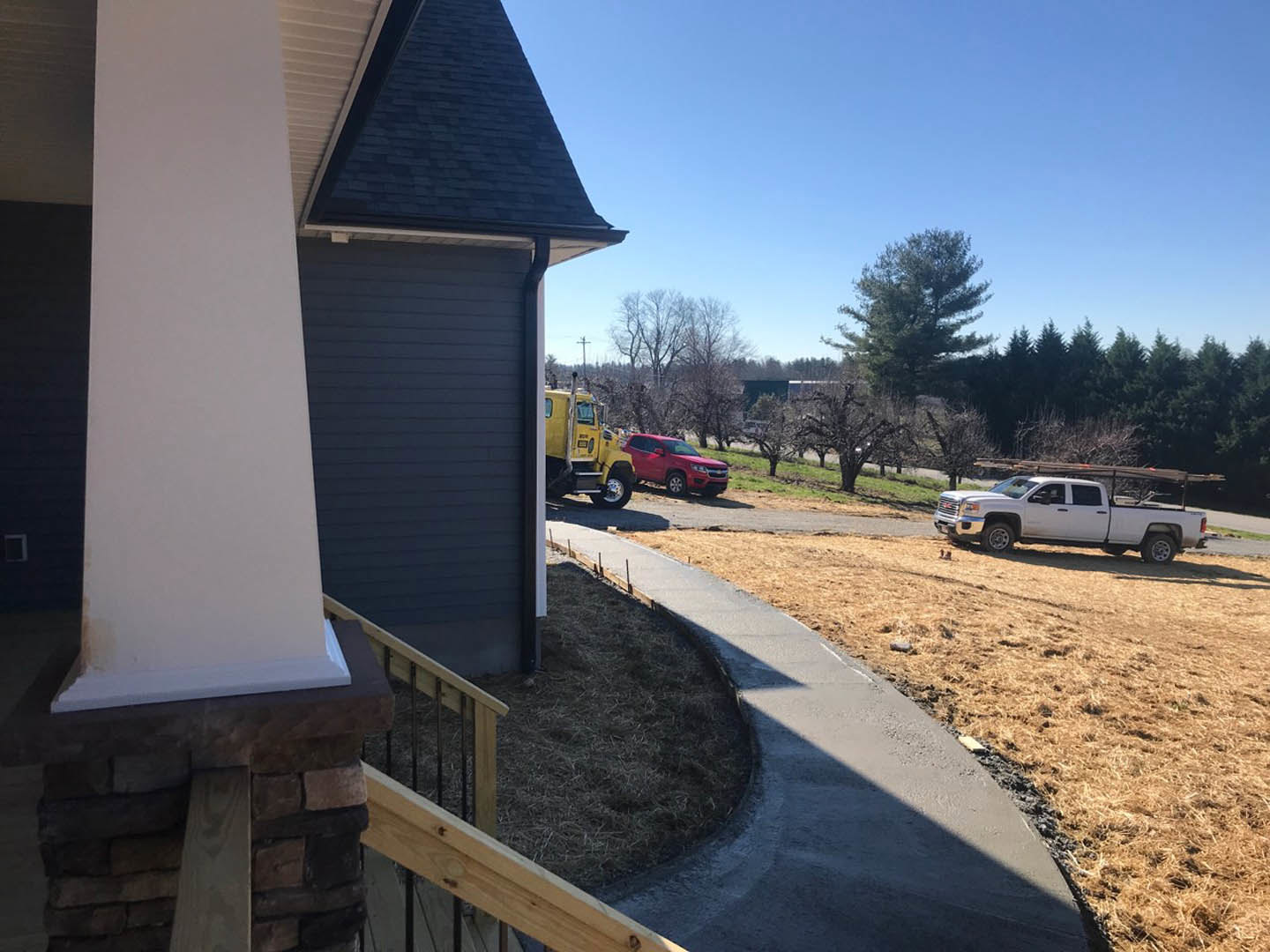 Stone exterior custom home with blue accent wall, concrete sidewalk, grassy yard, and several parked vehicles including a white truck, red car, and yellow truck.