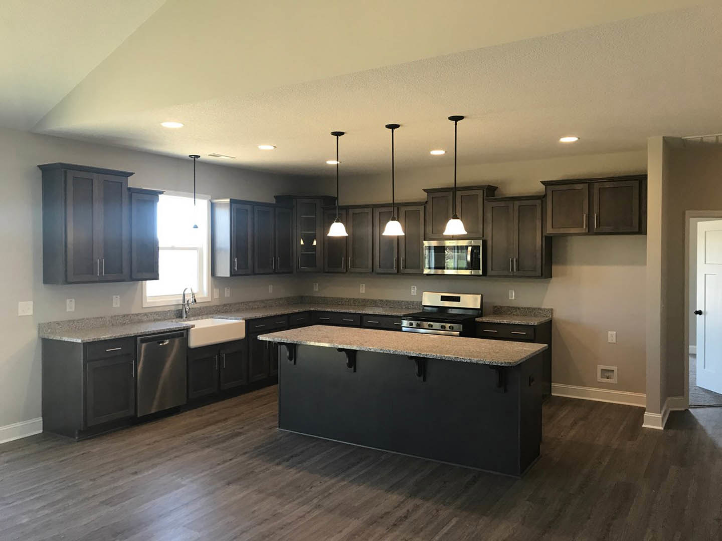 Kitchen with dark wood cabinets, large central island with granite countertop, stainless steel sink, tile backsplash, and hardwood flooring