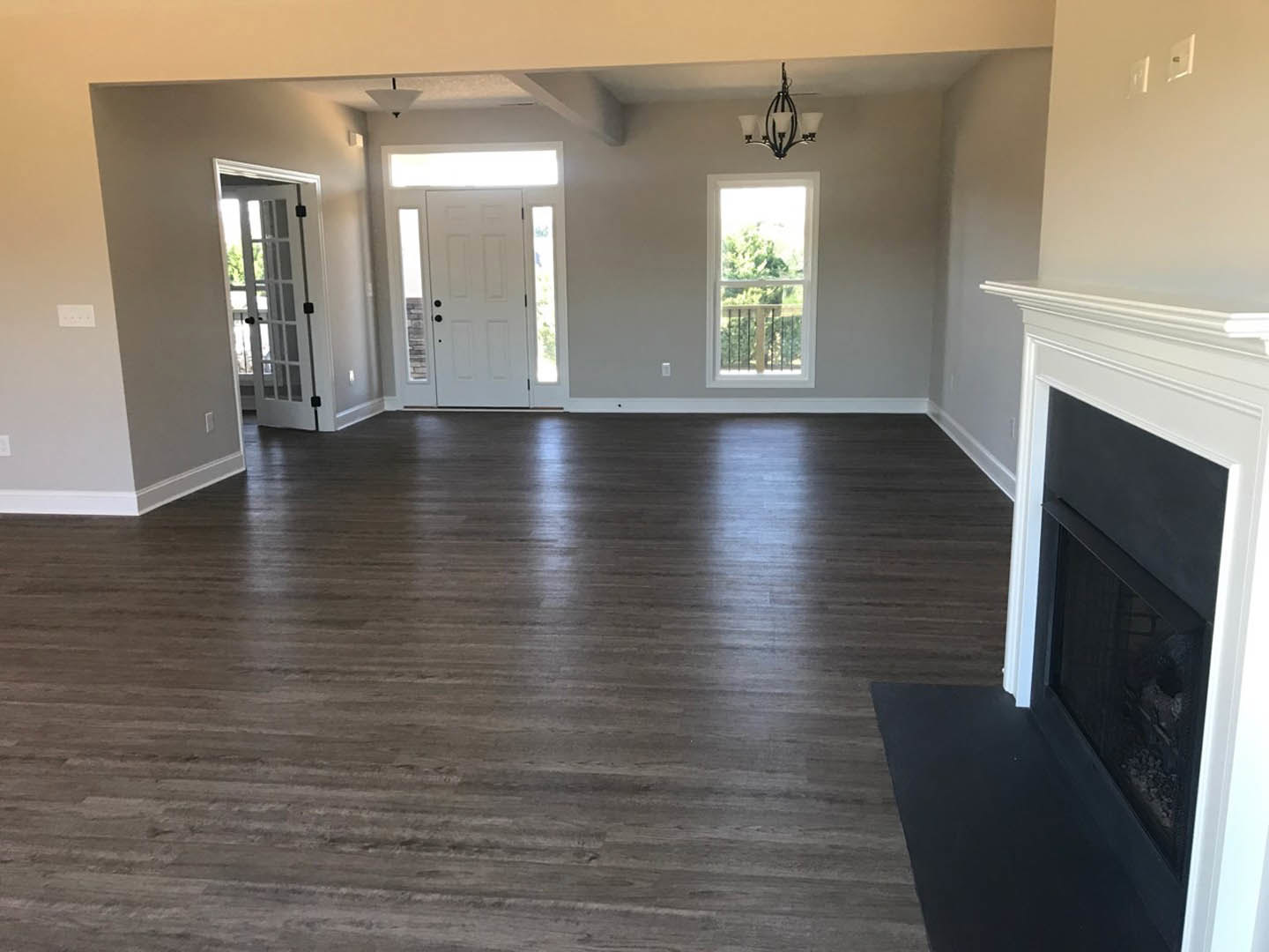 Living room featuring hardwood floors, white fireplace with mantel, glass-paneled door, large window with railing overlooking trees, white walls with crown molding