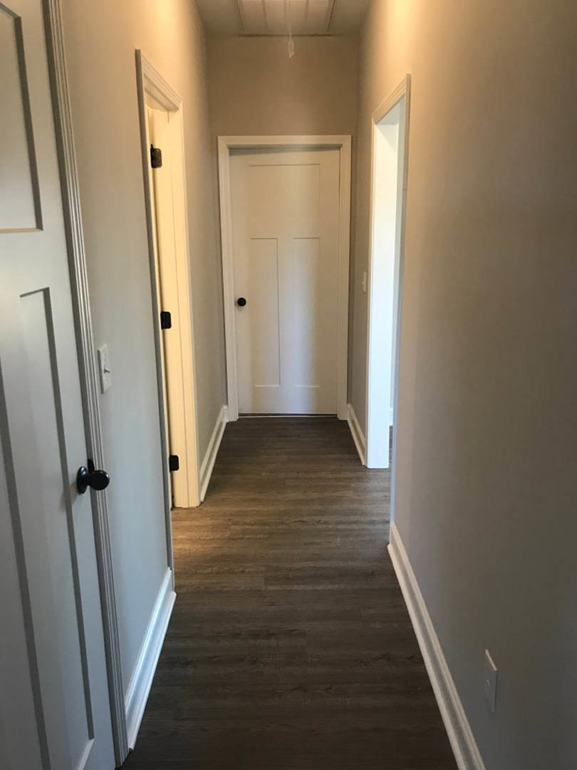 Hallway with white paneled doors, black door knobs, wood laminate flooring, white plaster walls, ceiling light fixture