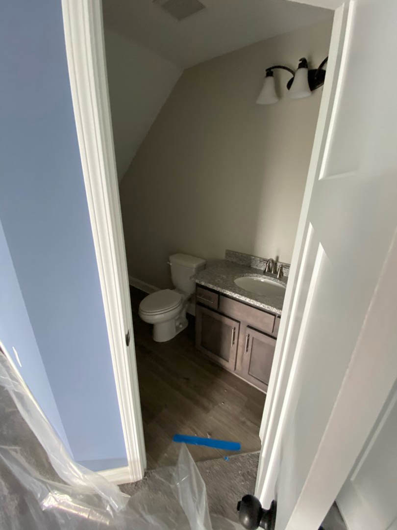 Modern bathroom with white toilet, rectangular sink on a light stone countertop, neutral plaster walls, and light tile flooring
