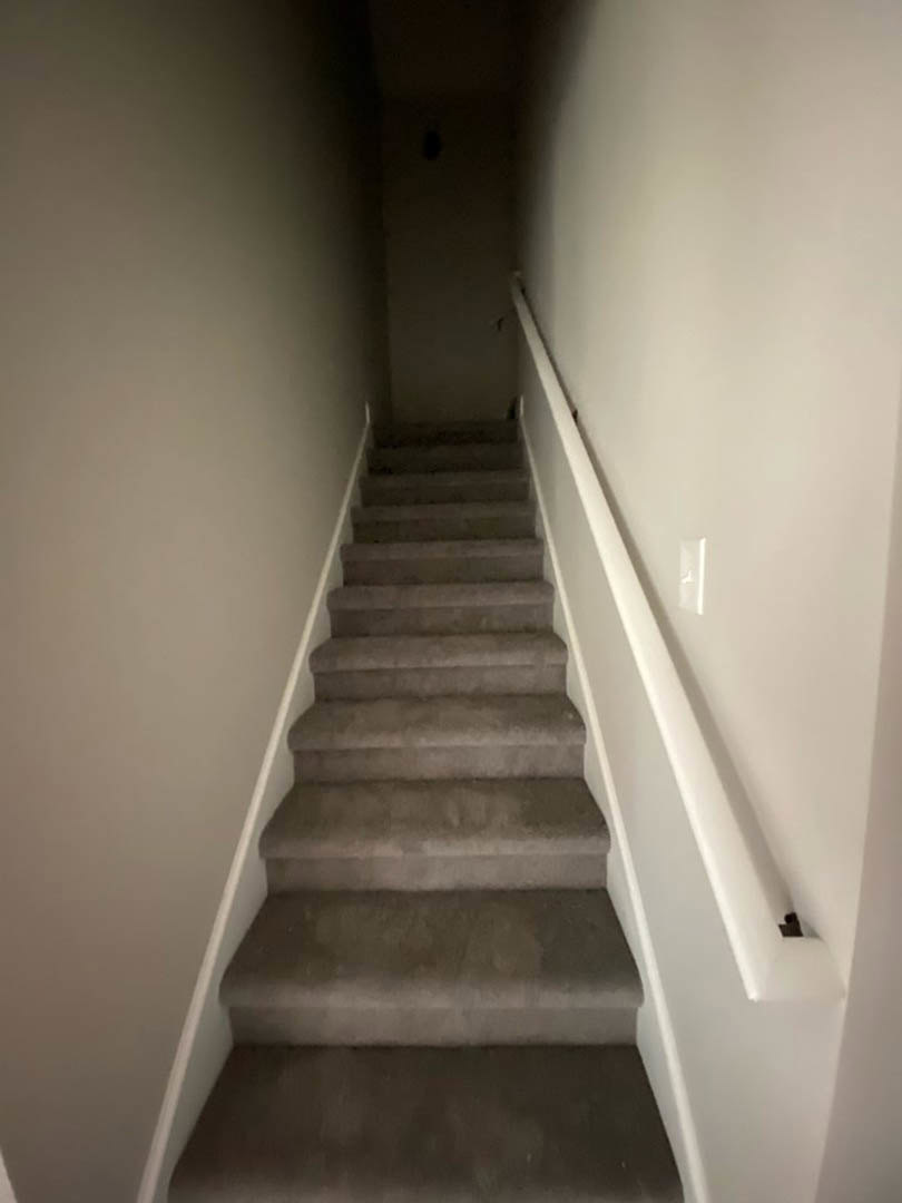 Wood staircase with metal handrail, plaster walls, open door at landing, light hardwood flooring