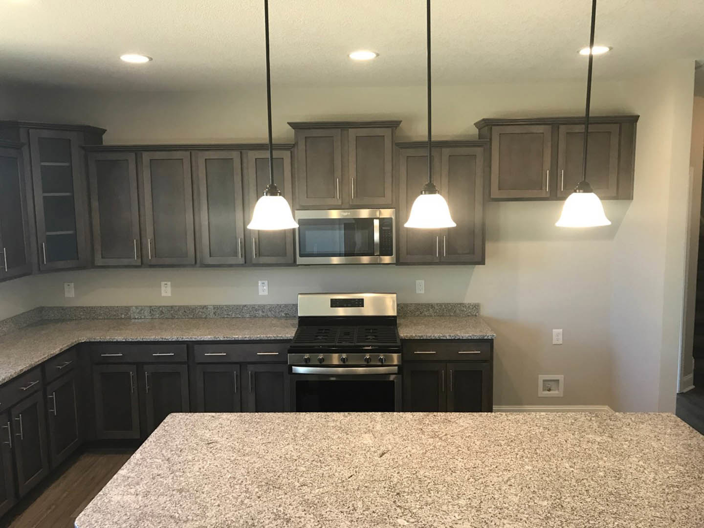 Kitchen with marble countertops, white cabinetry, stainless steel stove and microwave, tile flooring, and a white outlet on the backsplash wall