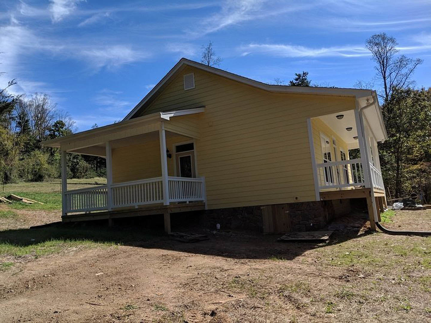 Yellow siding house with white porch railing, gabled roof, front porch, grassy yard, and mature tree nearby.