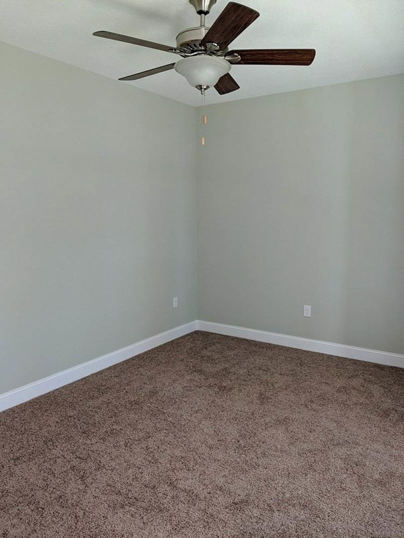 Ceiling fan with integrated light fixture mounted on white plaster ceiling above brown carpeted floor and white baseboards in a residential room