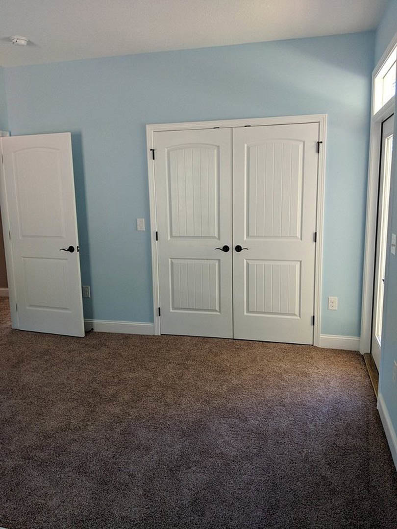 Carpeted room featuring a white double door with black handles and a single white door with a black handle, surrounded by smooth plaster walls.
