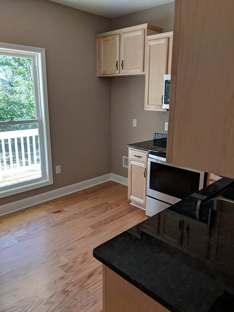 Kitchen with wood flooring, black countertops, white cabinetry, stainless steel appliances, and a window with a white railing