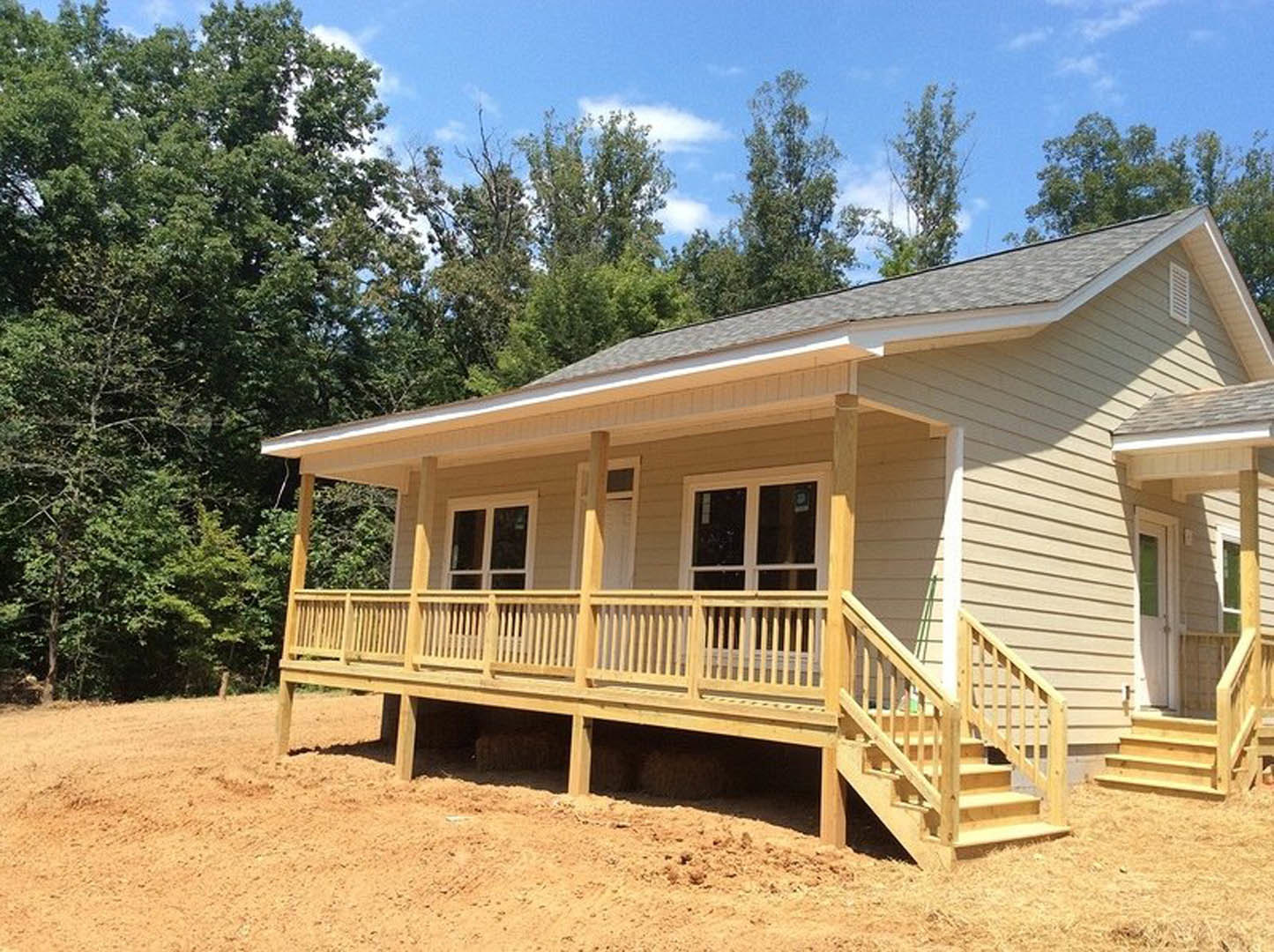 Wood-clad home with two covered porches, wooden stairs, large windows, and a shingled roof surrounded by mature trees.