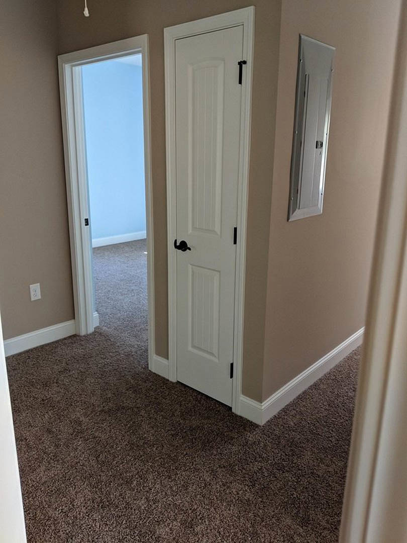 White paneled door with black handle set in a carpeted room, white baseboard trim and smooth plaster walls visible