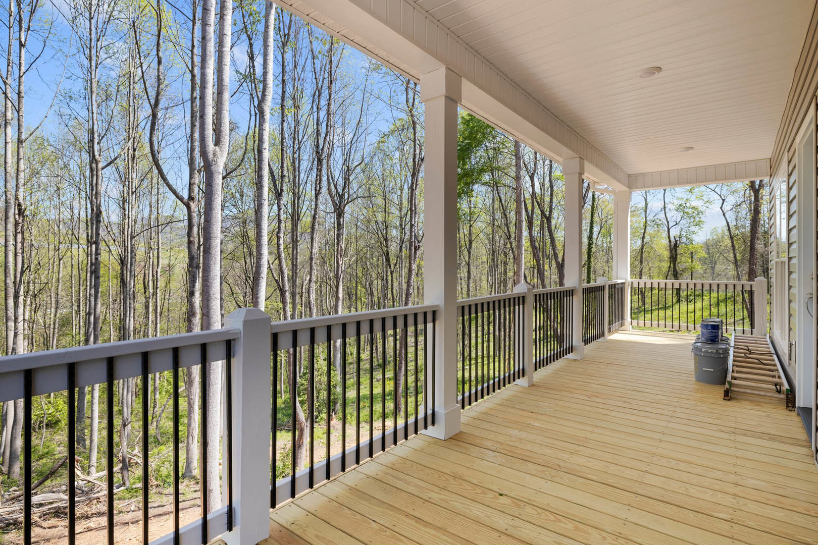 Wooden deck with horizontal railing, stacked paint buckets, and leafy trees in the background
