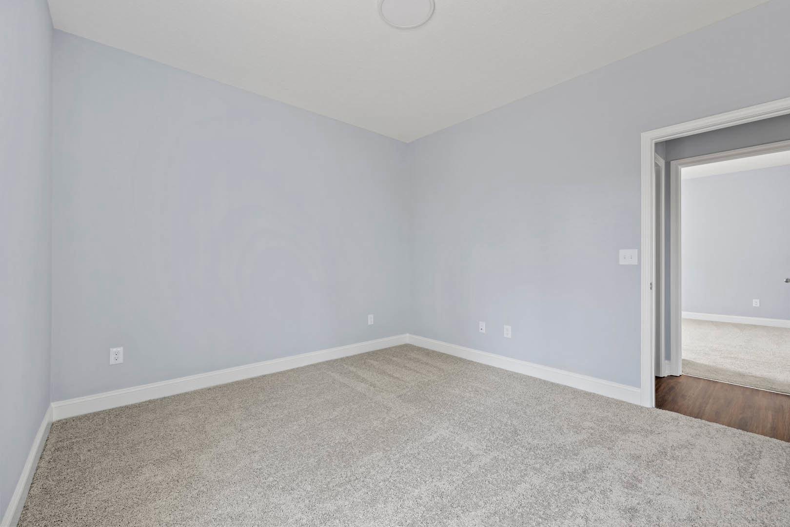 Carpeted bedroom with white walls, open door, and round white ceiling light fixture