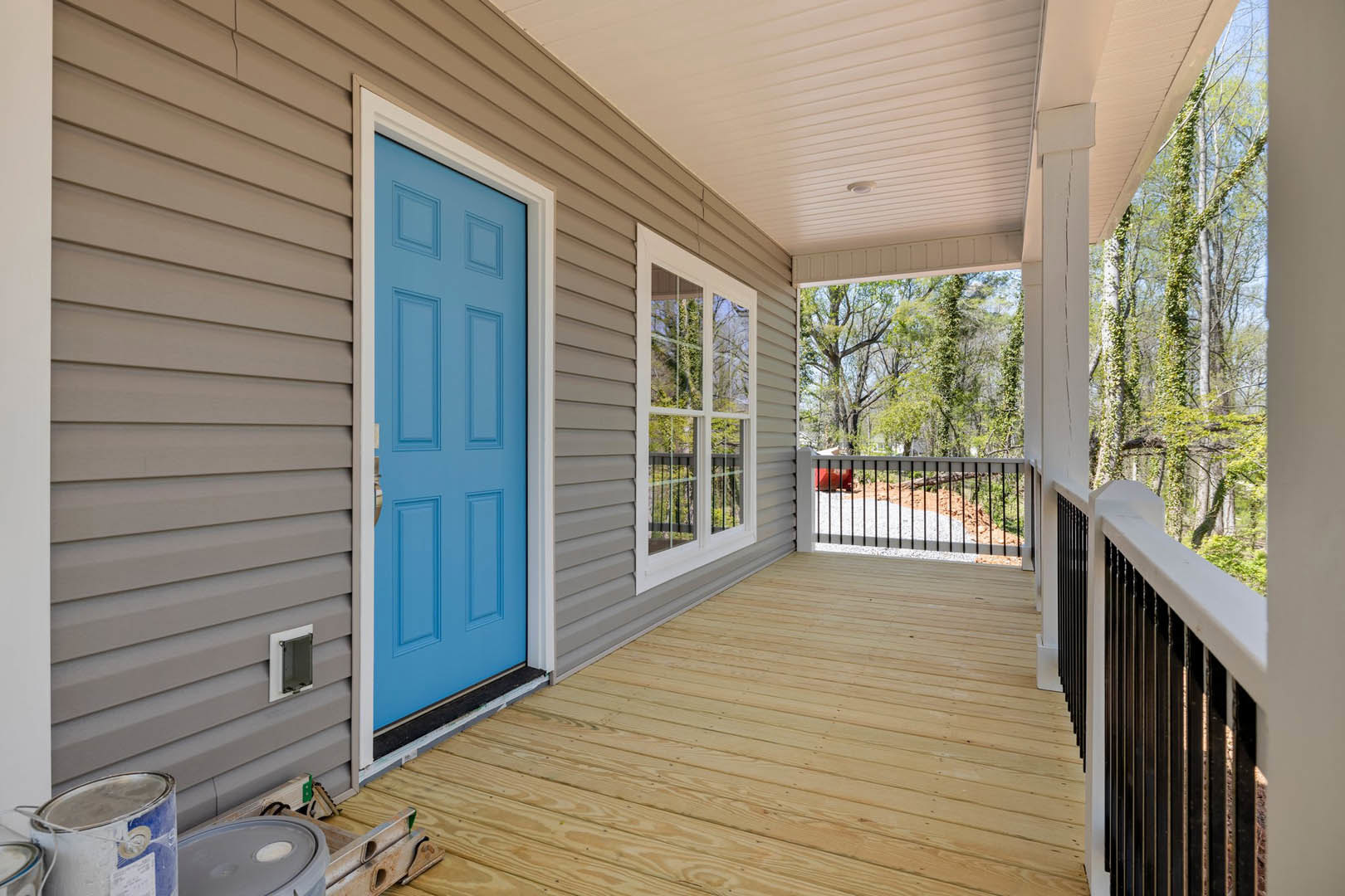 Wooden porch with metal railing, blue door framed in white, large windows, and light-colored deck flooring