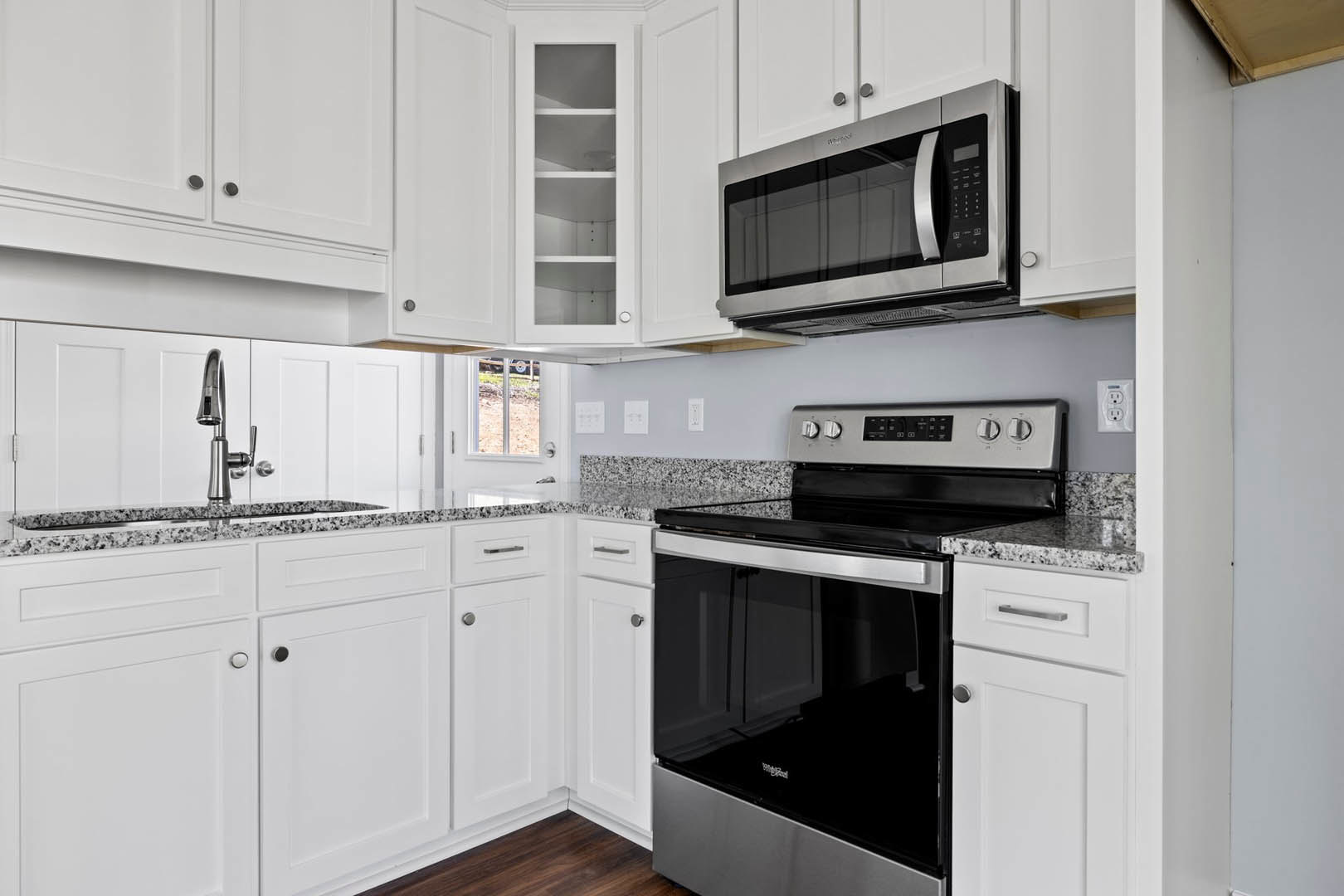 White kitchen cabinets with black stove, oven, and microwave; chrome faucet over light countertop; open shelving and smooth cabinet fronts.