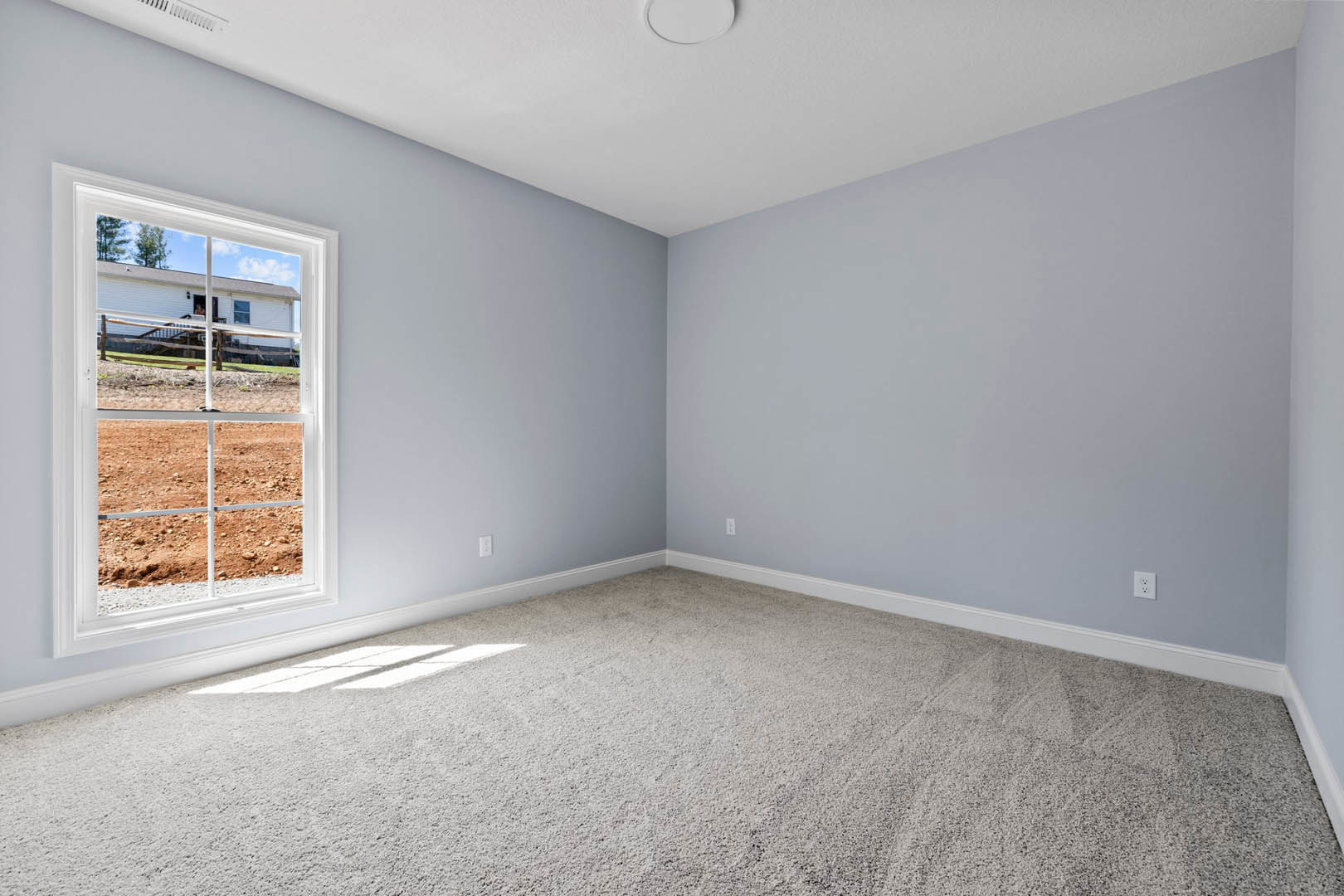 Carpeted room with white walls, large window overlooking dirt field, white ceiling featuring recessed light fixture