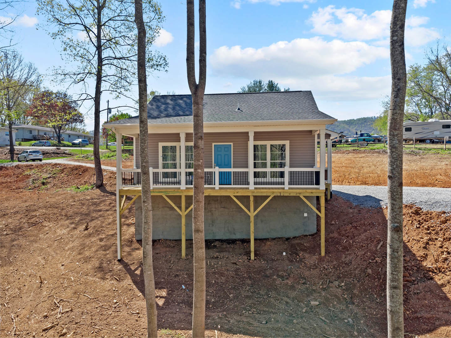 Two-story house with blue front door, white picket fence, covered front porch, side porch, gabled roof, large windows, and mature tree in landscaped yard