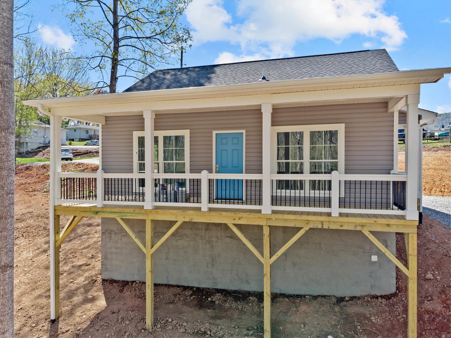 Front porch with white railing, blue entry door, large window, and leafy tree in foreground