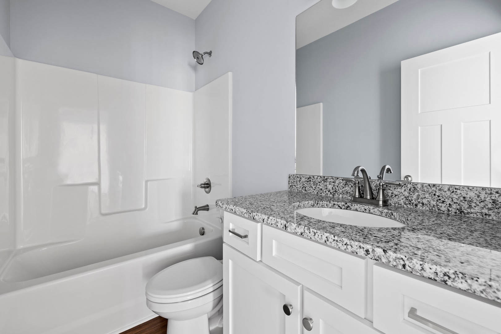 Bathroom with marble countertop, white bathtub, closed toilet, wall-mounted shower head, white door, and light fixture