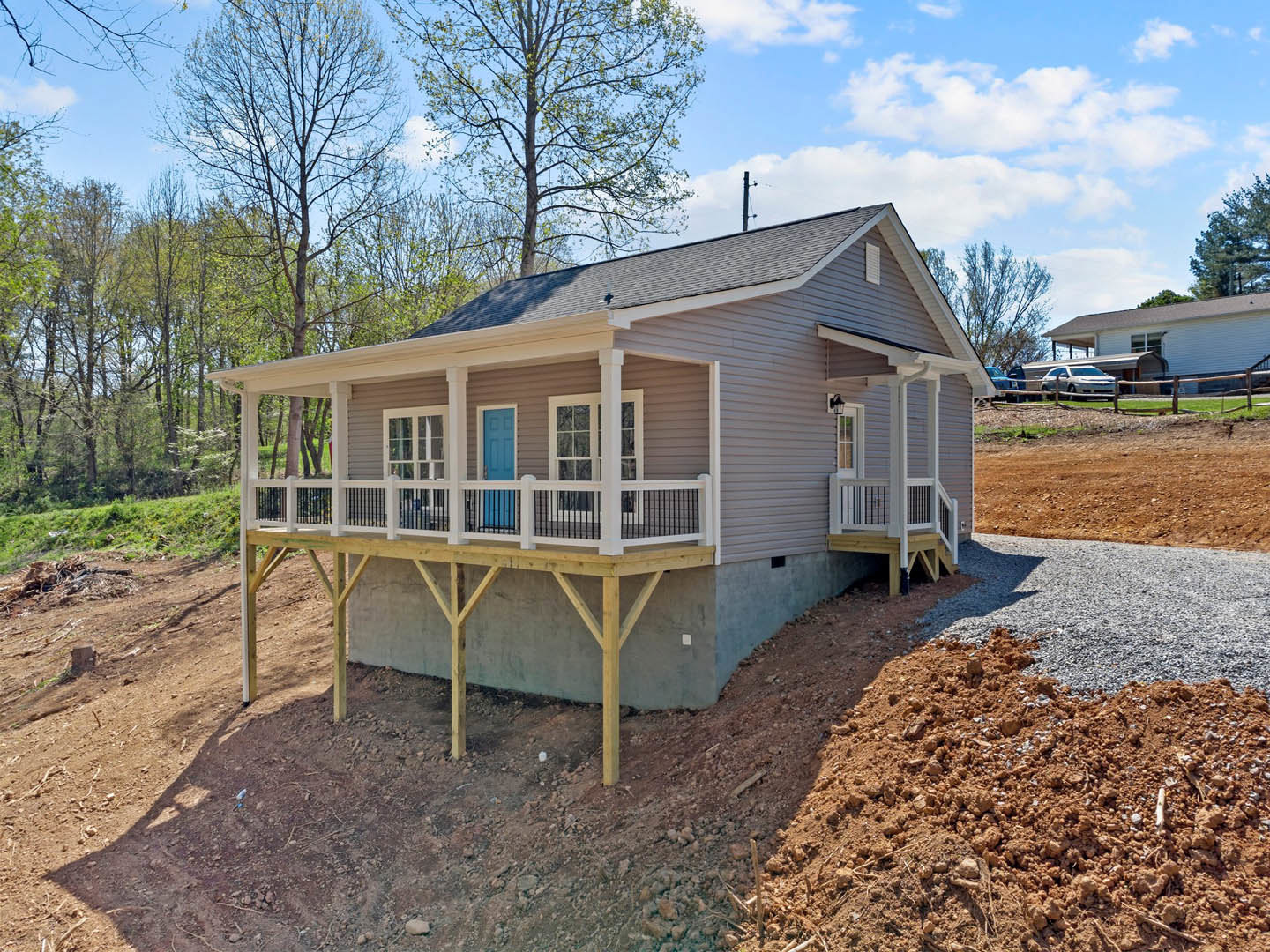 Two-story house with white porch railing, gravel path leading to entrance, large window with white trim, bare tree in front yard, cloudy sky overhead