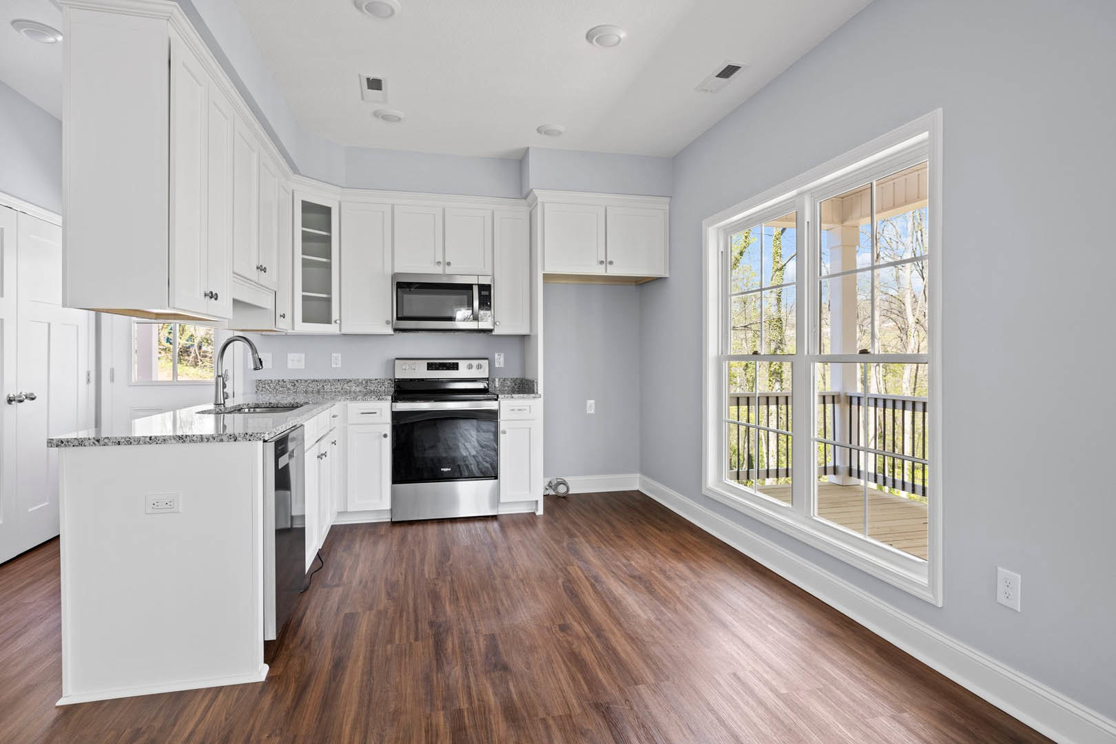Kitchen with wood flooring, white cabinetry, stainless steel stove, window overlooking trees and porch, light switch on wall