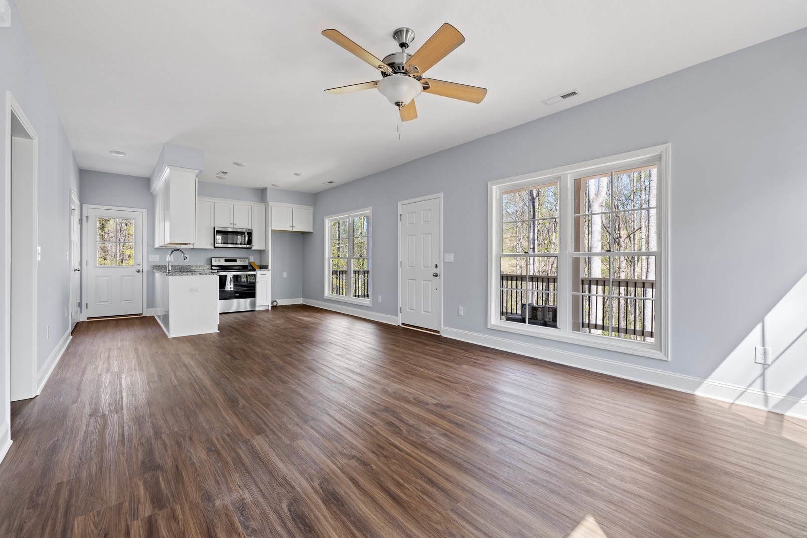 Hardwood floor room with ceiling fan, white door with silver handle, window showing trees, built-in microwave