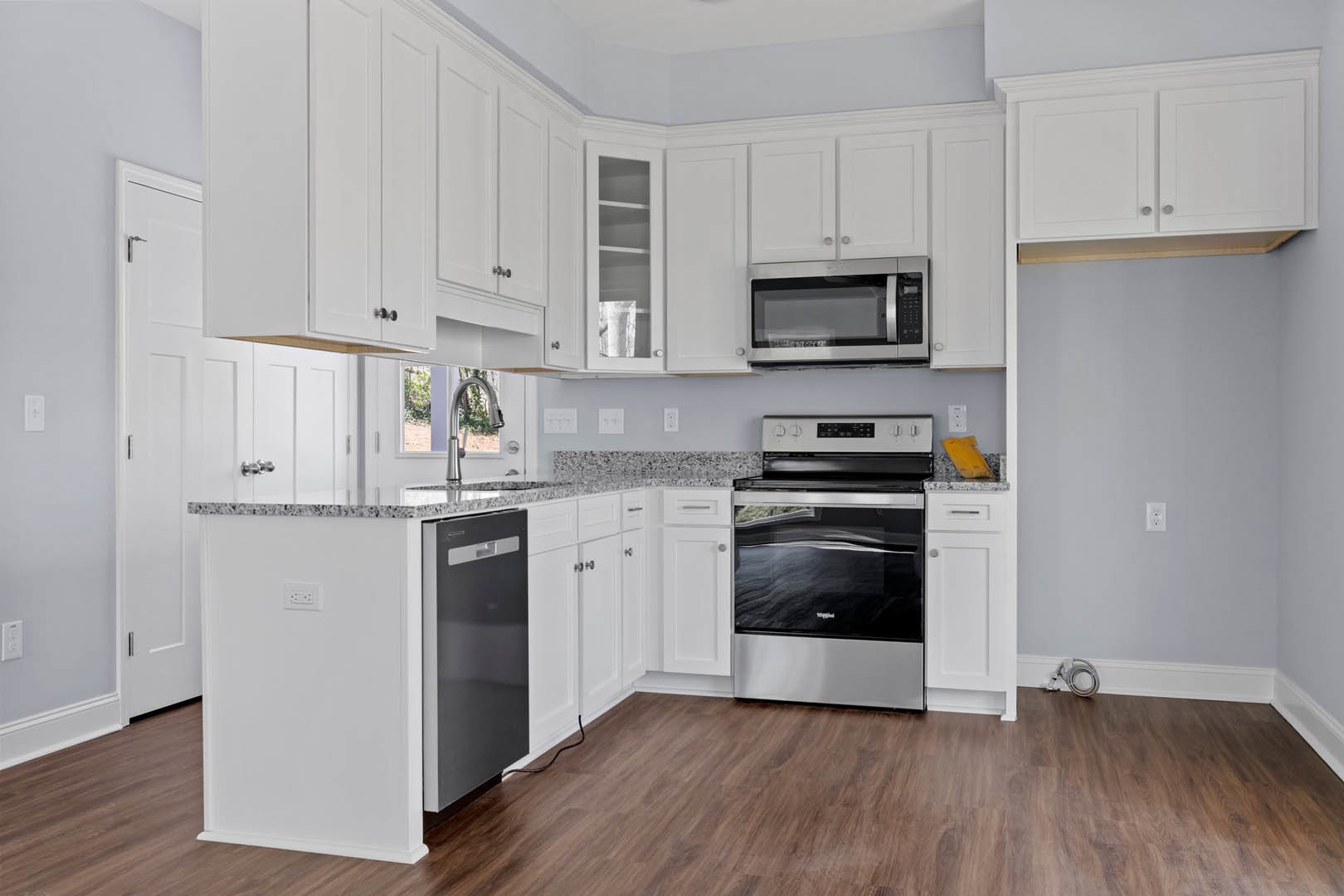 White kitchen cabinets, black stove and microwave, wood flooring, black cord visible near baseboards