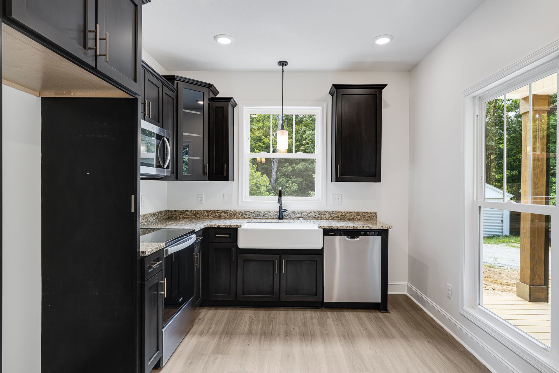 Black kitchen cabinets with stainless steel sink, white countertops, built-in dishwasher, white walls, window with natural light, black door with white trim.