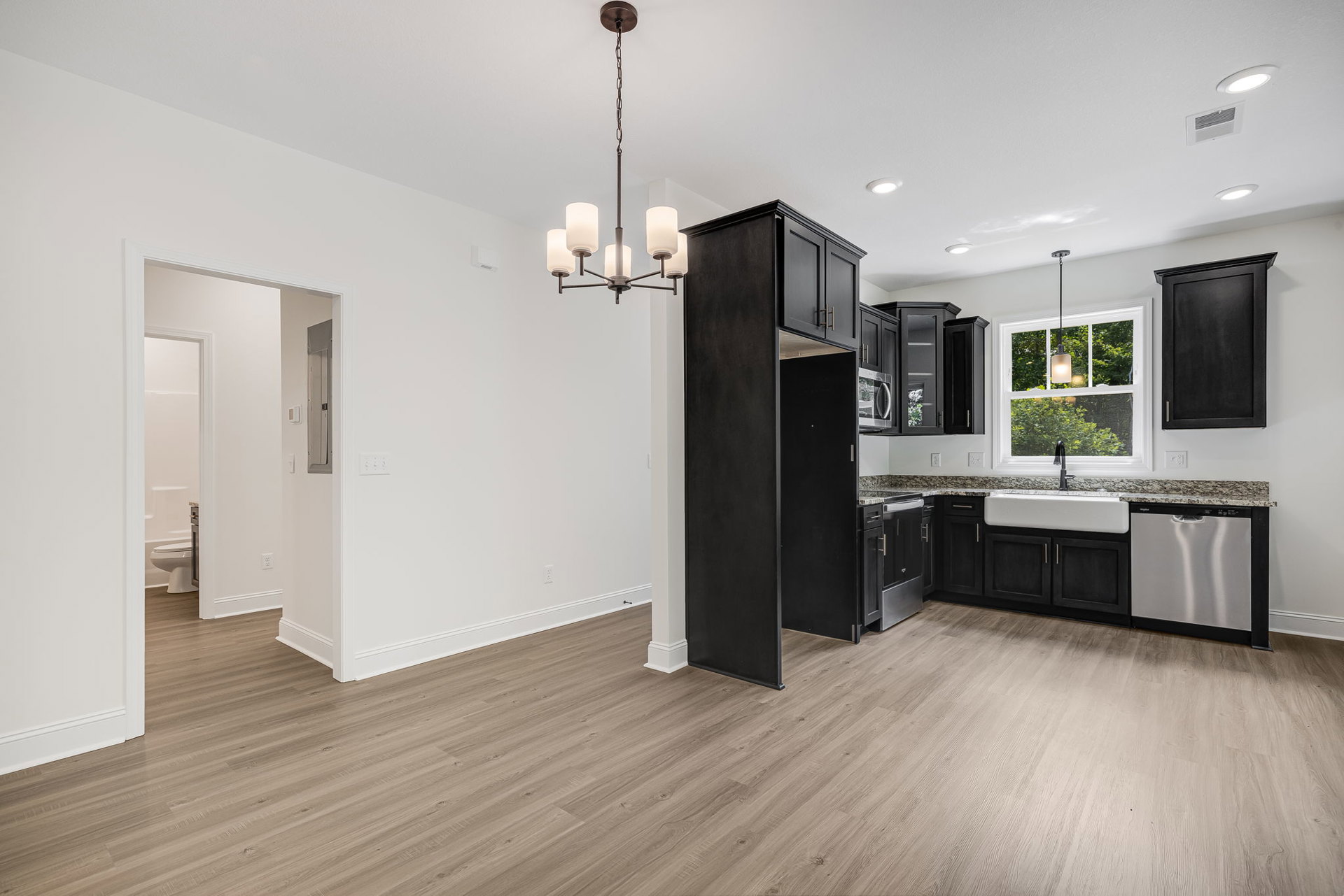 Open-concept kitchen and dining area featuring white cabinetry, stainless steel dishwasher, laminate flooring, and a modern chandelier suspended above the dining table.