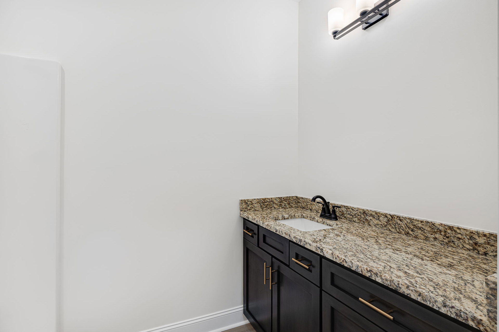 Marble countertop with black faucet, white sink, dark cabinetry, and white walls with black trim in a modern bathroom