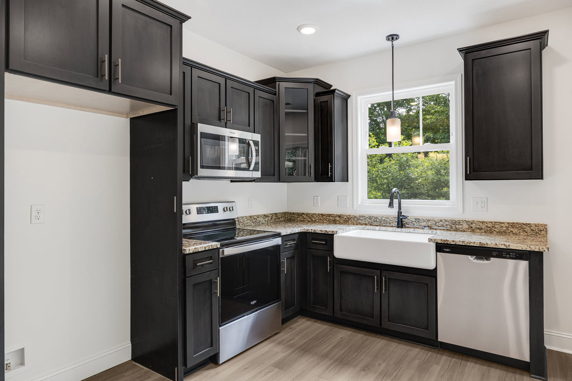 Kitchen featuring black cabinets, granite countertops, stainless steel microwave with glass door, black door with white trim, dishwasher with black handle, oven set beneath marble
