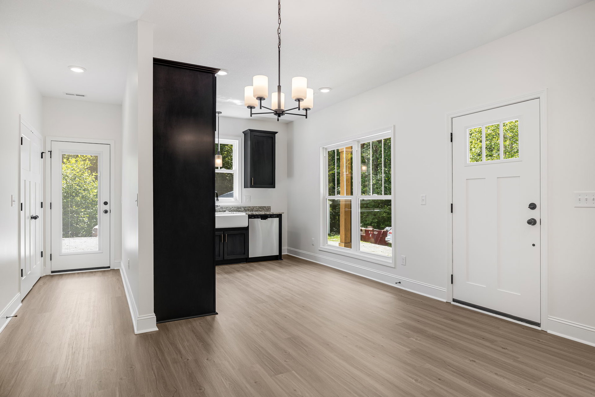 White walls, wood flooring, black door with white trim, white door with window, black board with mounted light, window framed by wooden post, hardwood finishes throughout.