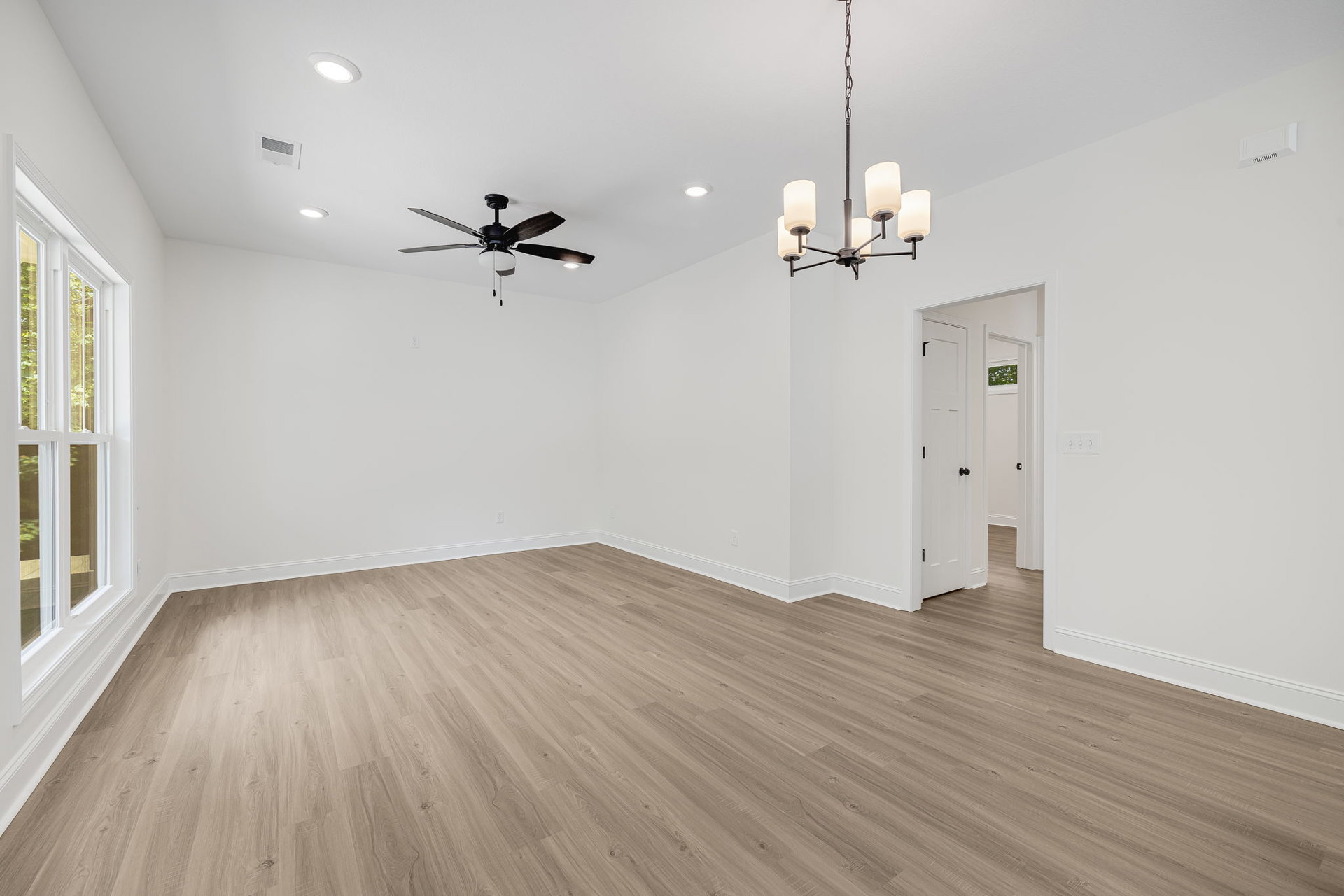 Ceiling fan with light fixture above wood laminate flooring, white plaster walls, and large window in residential interior