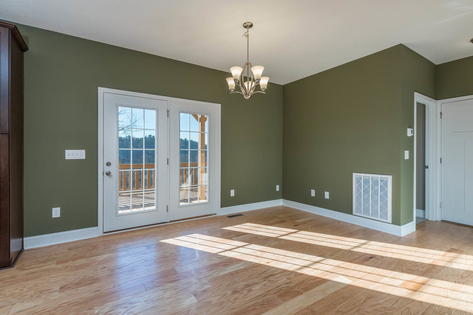 Green walls and wood flooring in a sunlit room, white double doors with glass panes, ceiling chandelier, decorative molding, and floor vent