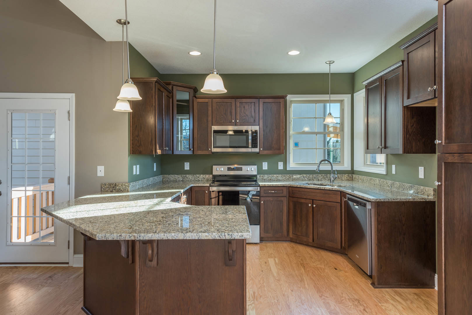 Kitchen with polished granite countertops, wood flooring, white cabinetry, stainless steel sink, and pendant light fixtures