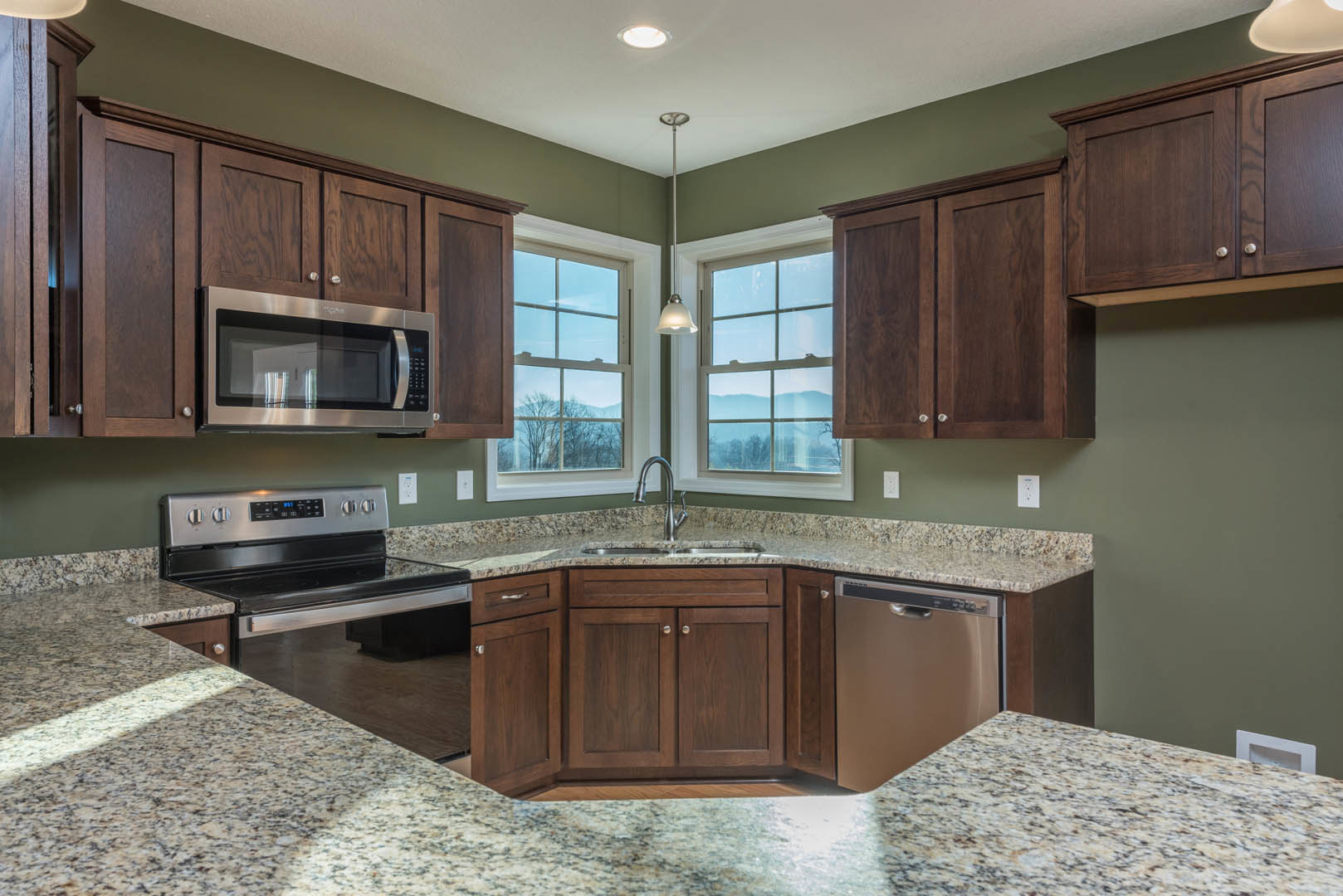 Granite countertops with undermount sink, stainless steel dishwasher, stove, microwave with glass, white cabinetry, window overlooking mountains