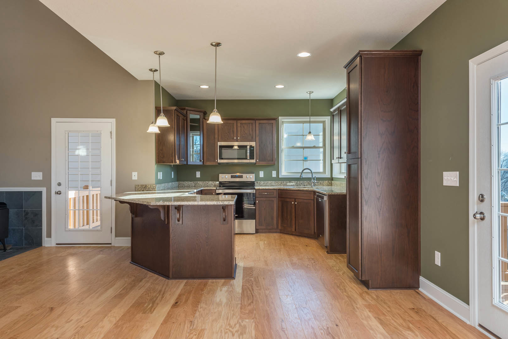 Kitchen with wood flooring, marble-topped island, white cabinetry, glass-paneled door, window above sink, and pendant light fixture