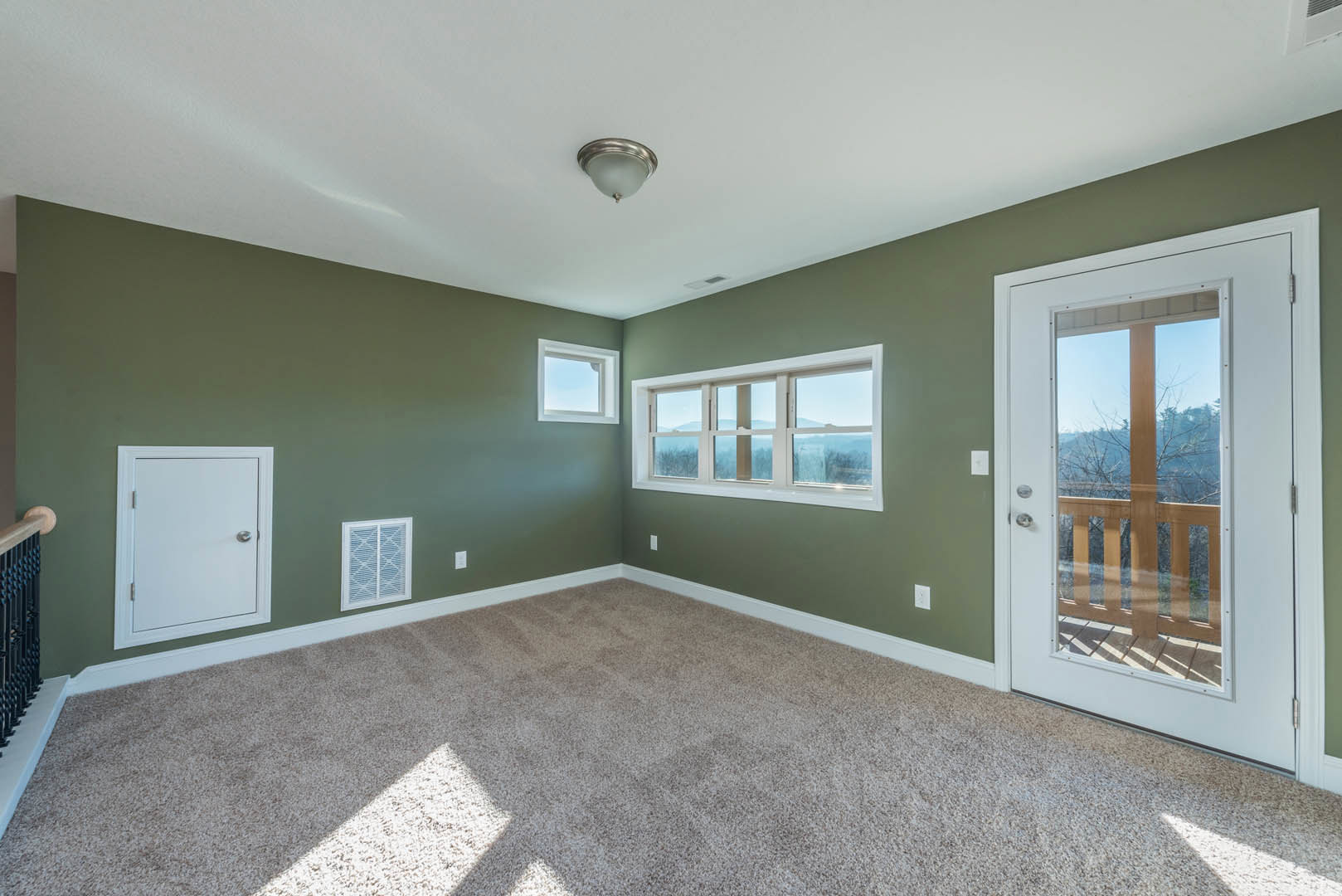 Carpeted room featuring a white door with silver knob, large windows showing mountain views and blue sky, smooth plaster walls, and white ceiling.