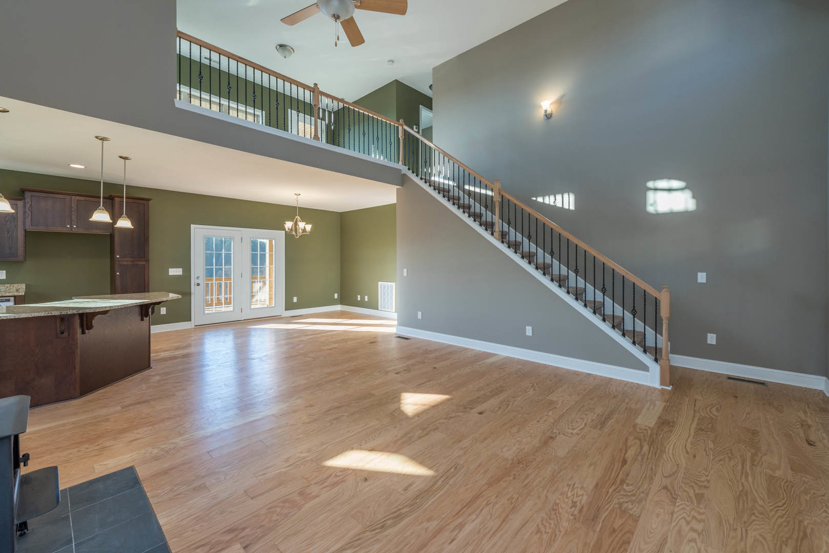 Spacious room featuring hardwood floors, a staircase with a dark railing, double glass-paneled doors, large windows, and a marble countertop