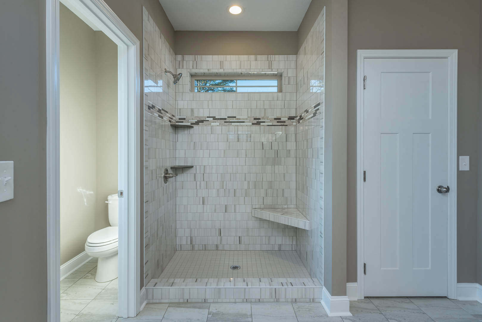 Modern bathroom featuring a glass-enclosed shower with a window, white tile walls, black and white tile flooring, a close-up of a white toilet, and a white door with a silver