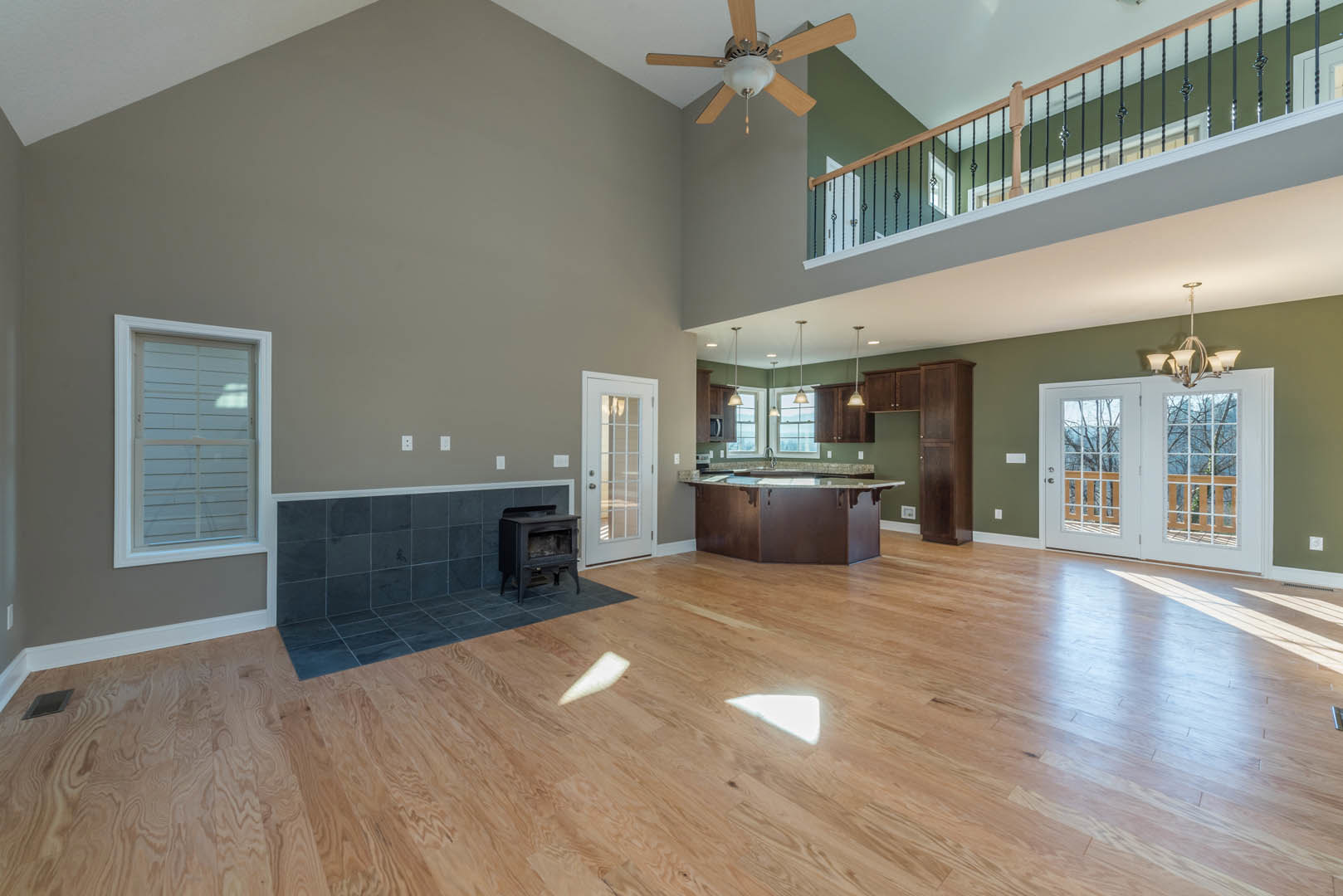 Spacious living room featuring hardwood floors, a black glass-door fireplace, open kitchen area, double glass-paneled doors, and large windows with balcony access