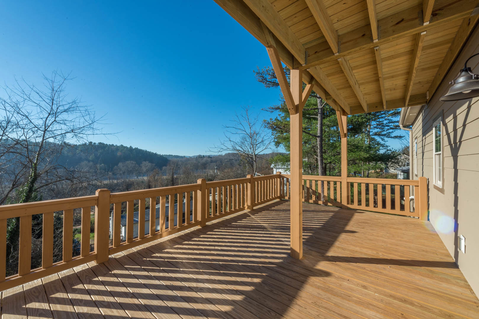 Wooden deck with railing and overhead beams, overlooking leafless trees and dense forest landscape under open sky
