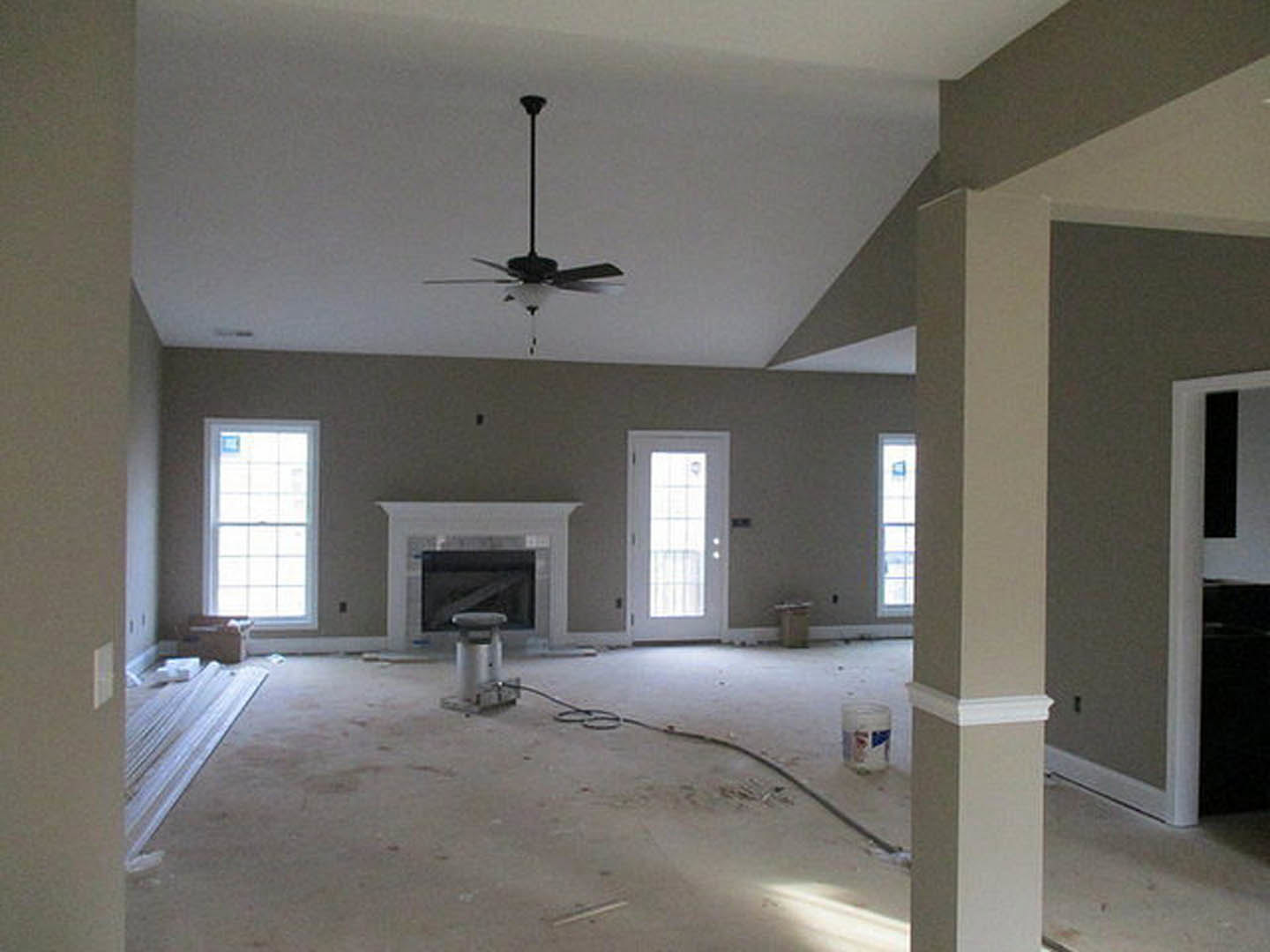 Living room with white-framed window, ceiling fan with light, plaster walls, and fireplace; hardwood flooring and neutral finishes.