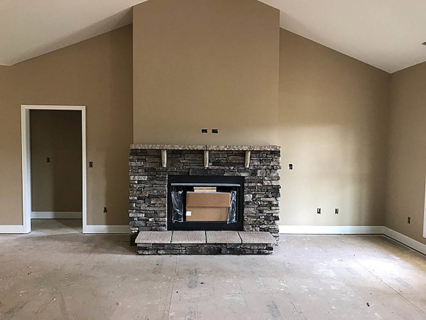 Modern living room with concrete floor and step, brick wall featuring black border, wood-burning stove set inside fireplace, light switch near doorway, and open shelving above