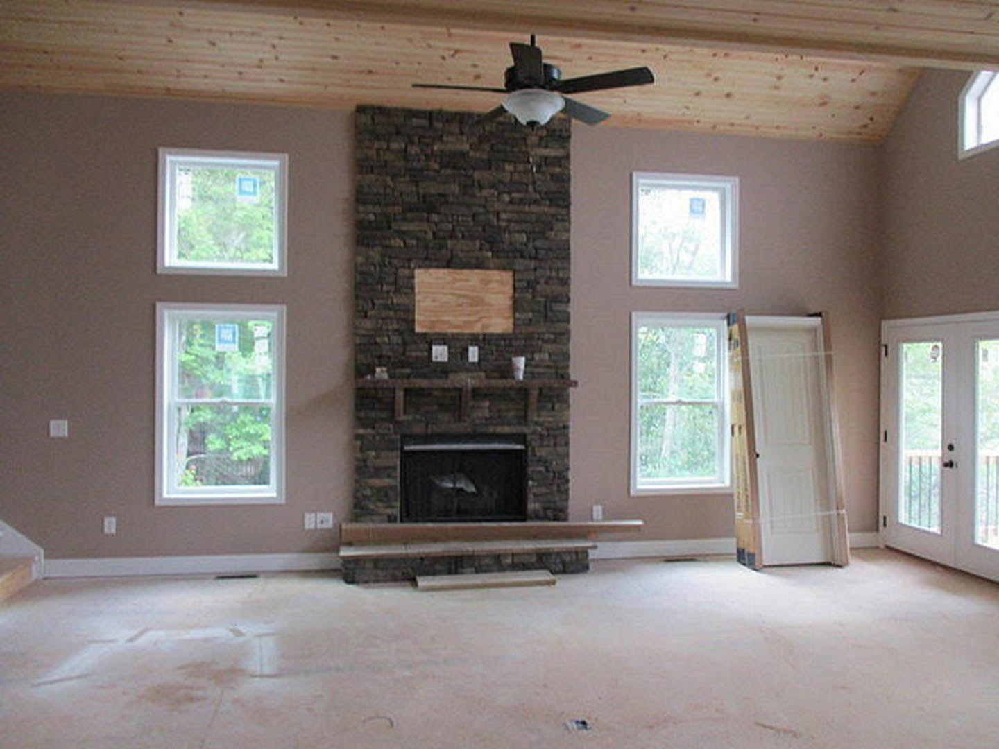 Living room with stone fireplace, ceiling fan with light, hardwood floors, large windows, neutral walls