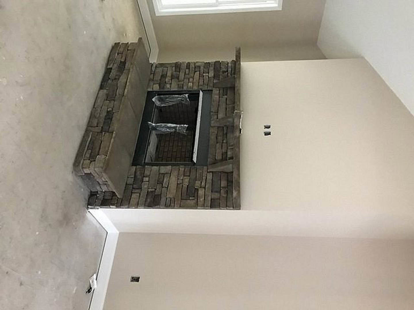 Brick fireplace set into plaster wall, hardwood floor, partial view of bathroom with sink, blurred hand in foreground