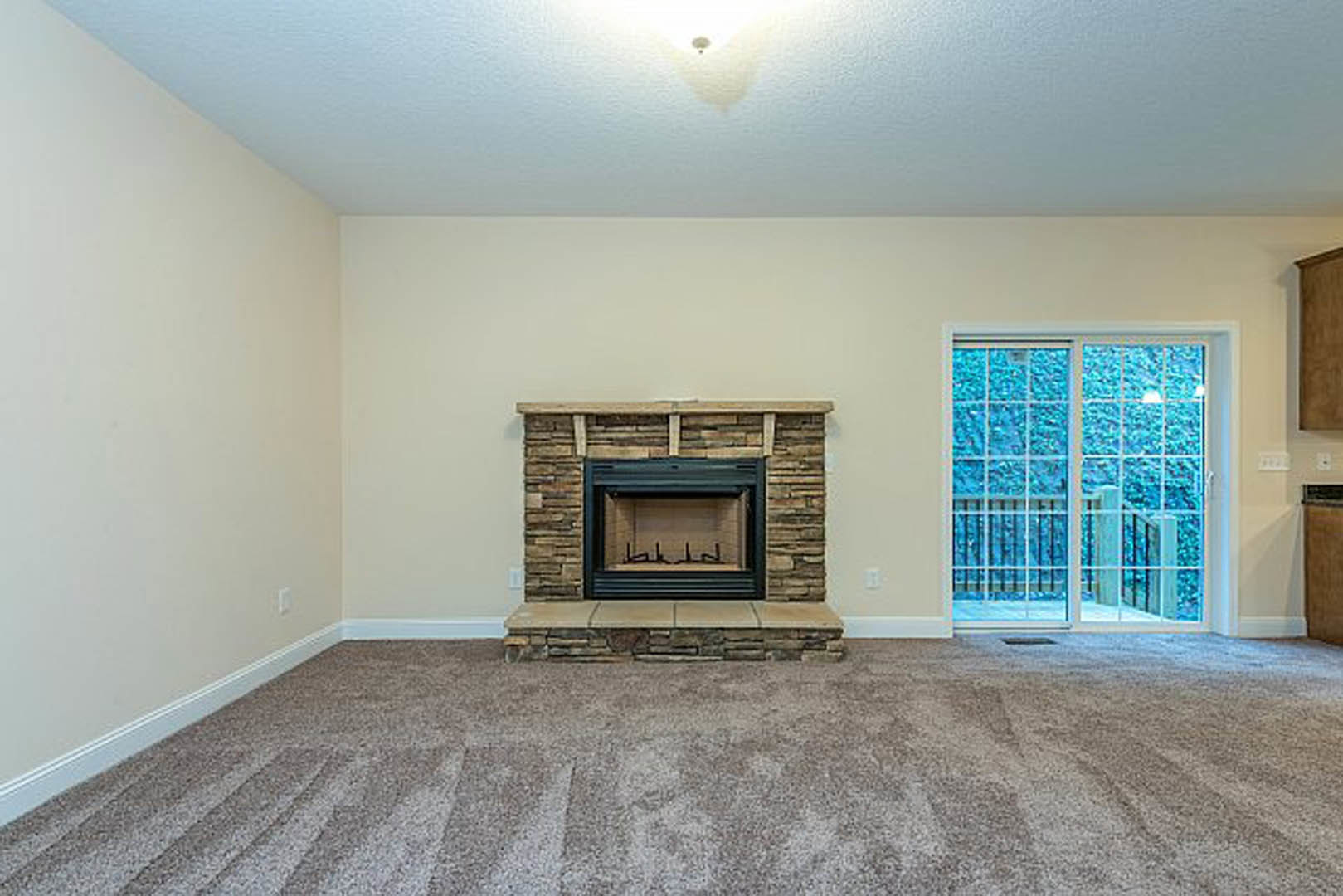 Living room with beige carpet flooring, brick fireplace set in a stone accent wall, sliding glass door with metal railing, plaster walls, and hearth.