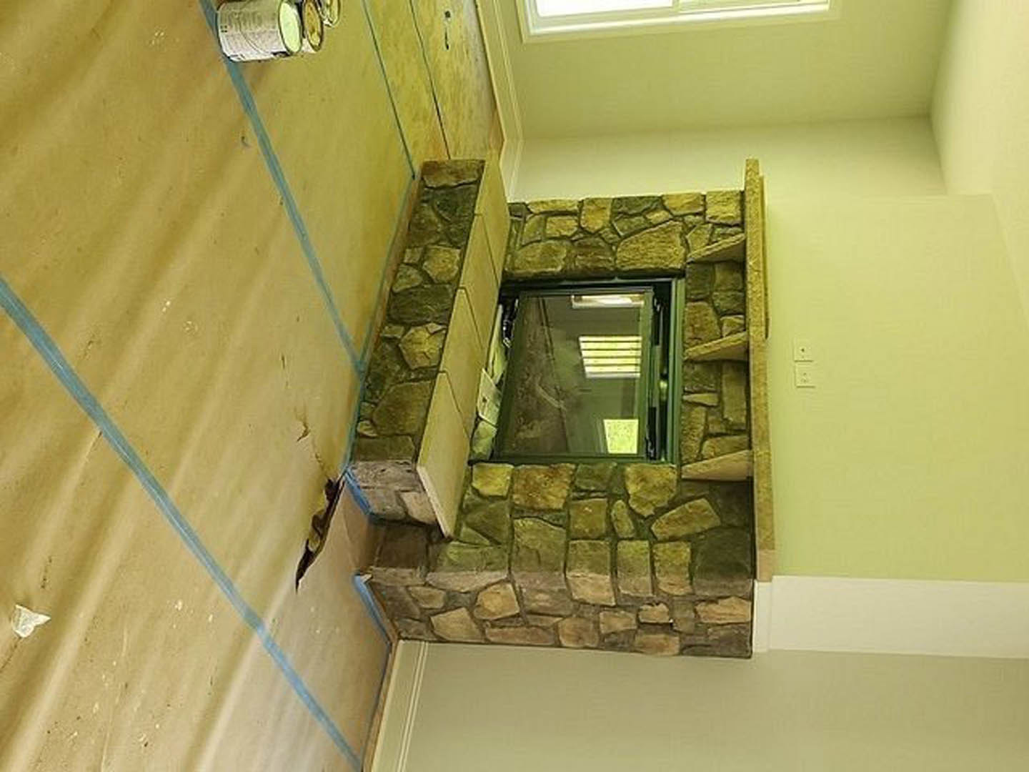 Stone fireplace with white plaster surround, rectangular window, light wood floor, and neutral walls in a modern living room