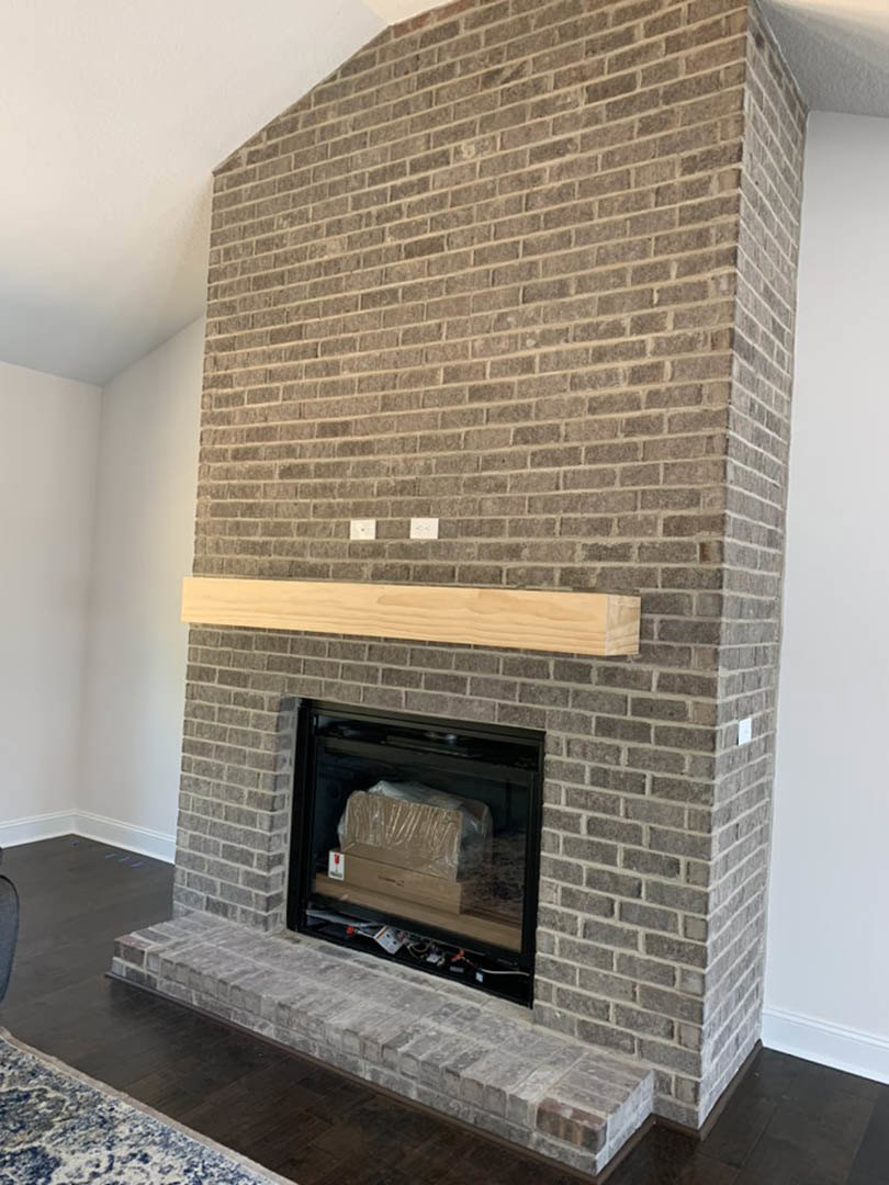 Brick fireplace with wood beam mantel, wood floor, and fire screen in a living room.