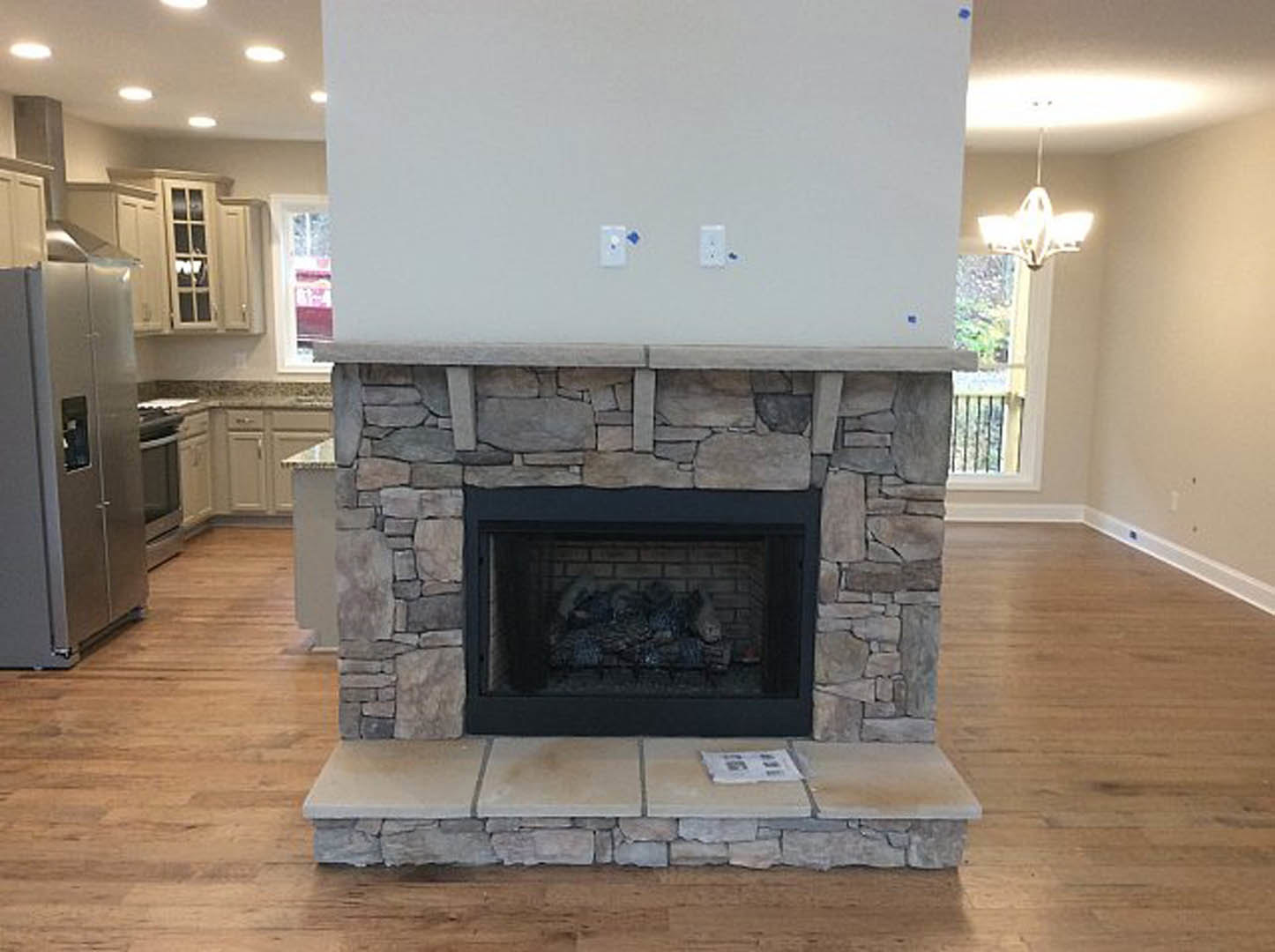 Stone fireplace with brick surround, black fire screen, and wood mantel in living room with hardwood flooring